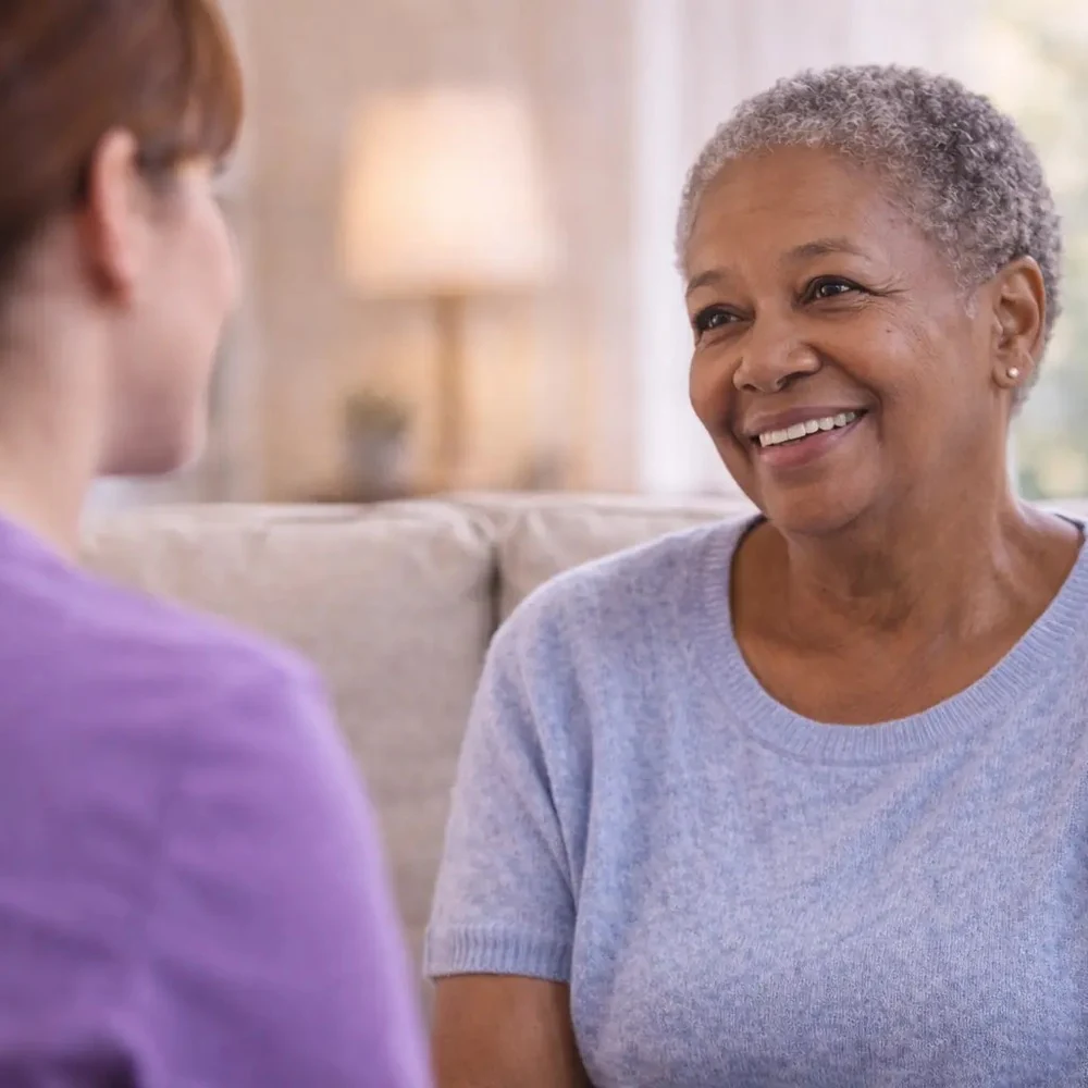 A smiling older patient talking with a nurse in purple scrubs